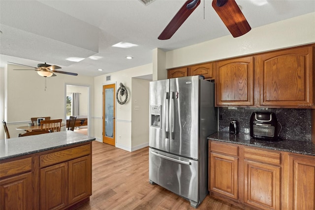 kitchen with stainless steel refrigerator with ice dispenser, light hardwood / wood-style floors, tasteful backsplash, and dark stone counters