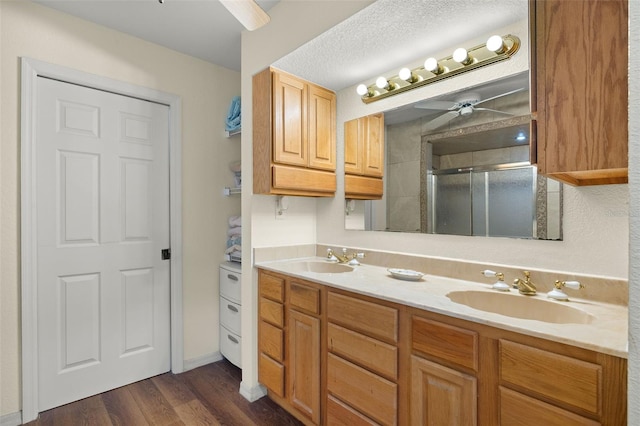 bathroom with ceiling fan, wood-type flooring, a textured ceiling, a shower with door, and vanity