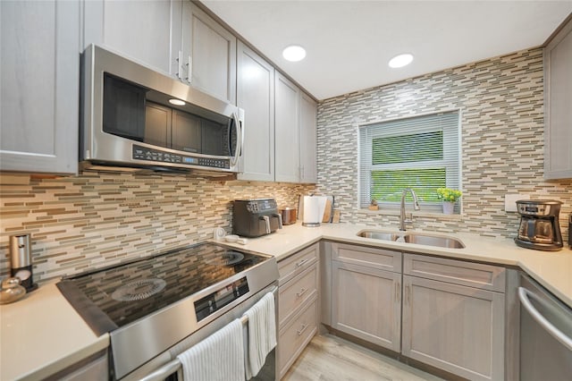 kitchen featuring decorative backsplash, stainless steel appliances, gray cabinets, and sink