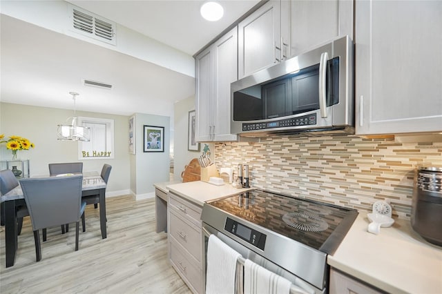 kitchen with gray cabinetry, tasteful backsplash, light hardwood / wood-style flooring, pendant lighting, and appliances with stainless steel finishes