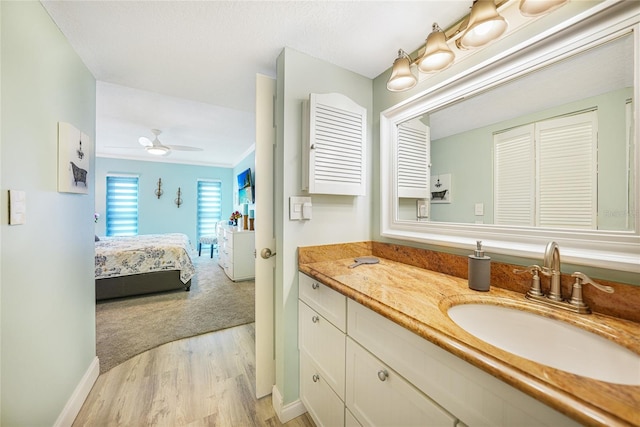 bathroom featuring ceiling fan, wood-type flooring, ornamental molding, and vanity