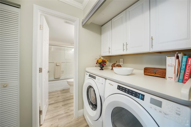 washroom featuring cabinets, light wood-type flooring, ornamental molding, and washing machine and clothes dryer