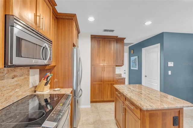 kitchen with light stone countertops, appliances with stainless steel finishes, tasteful backsplash, a center island, and light tile patterned flooring