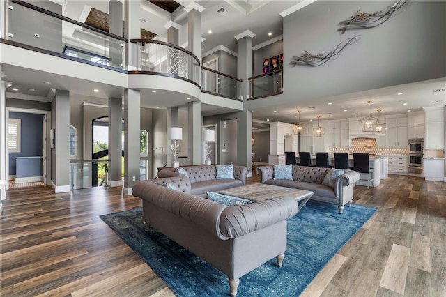 living room with a chandelier, wood-type flooring, a towering ceiling, and crown molding