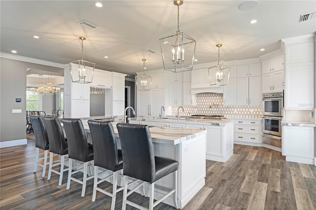 kitchen with double oven, crown molding, a spacious island, decorative light fixtures, and white cabinets