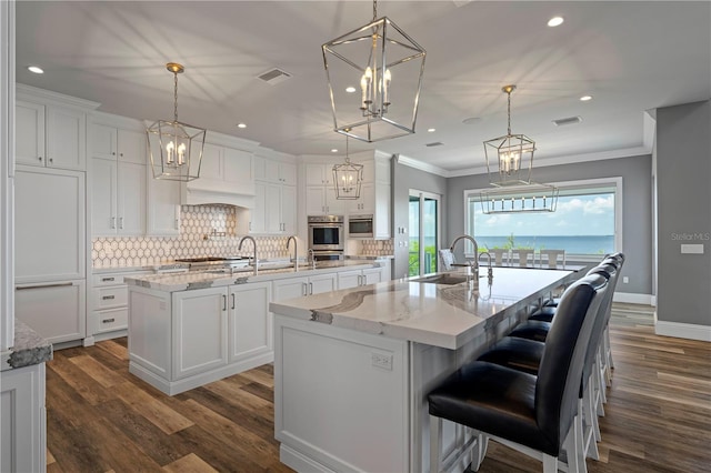 kitchen featuring sink, a large island with sink, decorative light fixtures, white cabinets, and dark hardwood / wood-style floors