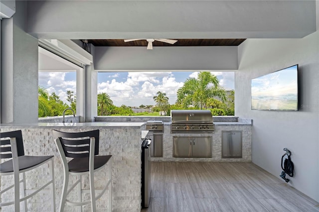 view of patio / terrace featuring grilling area, ceiling fan, an outdoor bar, and an outdoor kitchen