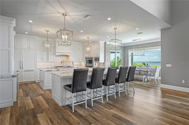 kitchen with dark hardwood / wood-style flooring, a center island with sink, white cabinetry, oven, and hanging light fixtures