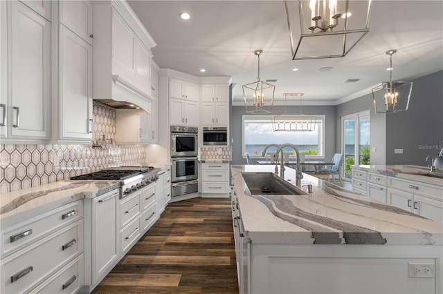 kitchen with appliances with stainless steel finishes, backsplash, decorative light fixtures, white cabinets, and an island with sink