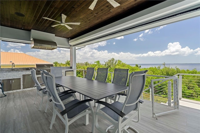 deck with ceiling fan, a grill, a water view, and an outdoor kitchen