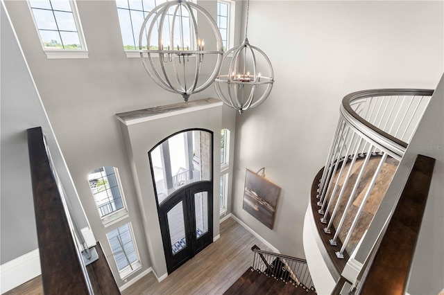 foyer entrance featuring a chandelier, wood-type flooring, a towering ceiling, and french doors