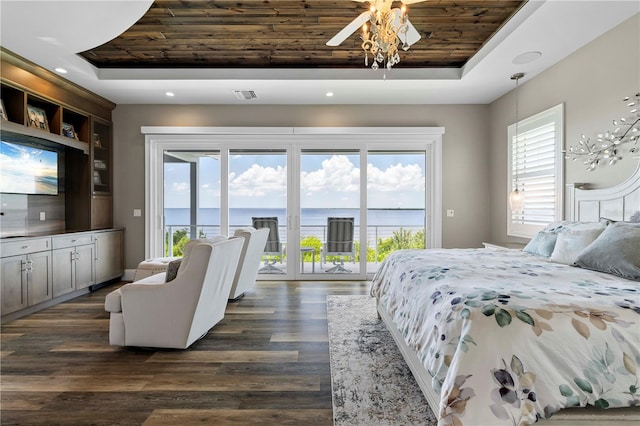 bedroom with a raised ceiling, dark hardwood / wood-style flooring, a water view, and access to outside