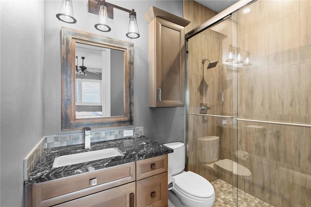 bathroom with ceiling fan, vanity, a shower with shower door, and toilet