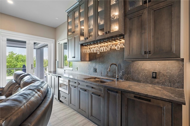 kitchen featuring backsplash, dark brown cabinets, sink, dark stone countertops, and stainless steel microwave