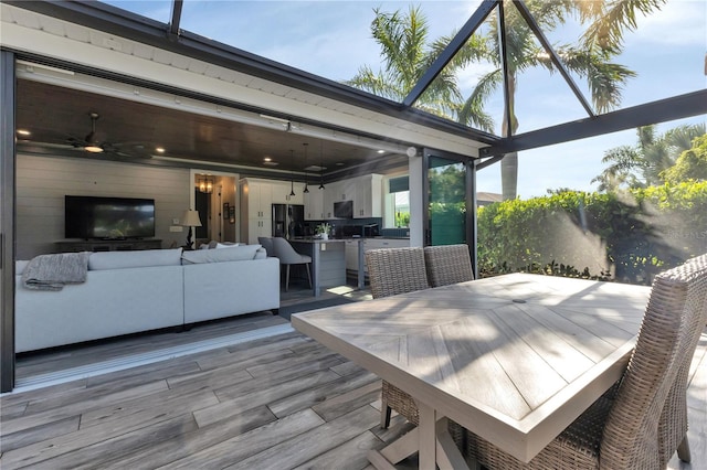 wooden terrace with an outdoor living space, glass enclosure, ceiling fan, and exterior kitchen