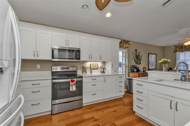 kitchen with ceiling fan, sink, stainless steel appliances, white cabinets, and light wood-type flooring