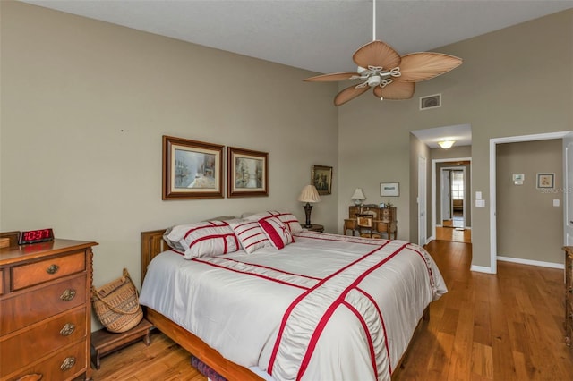 bedroom featuring ceiling fan, wood-type flooring, and a towering ceiling