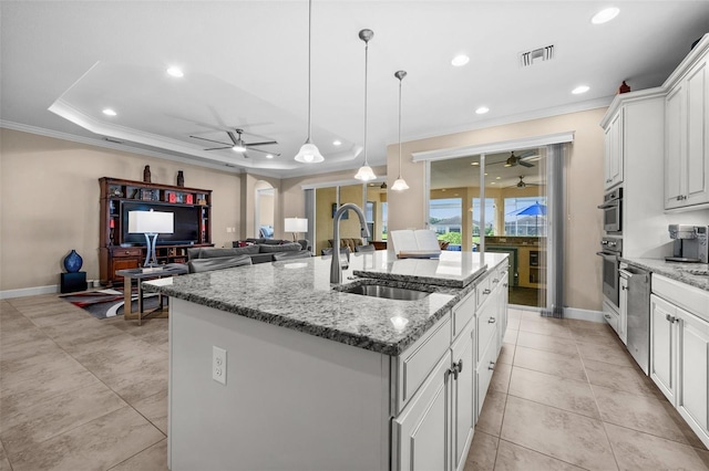 kitchen featuring sink, light stone counters, pendant lighting, a kitchen island with sink, and white cabinets