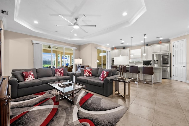 tiled living room with ceiling fan, ornamental molding, and a tray ceiling