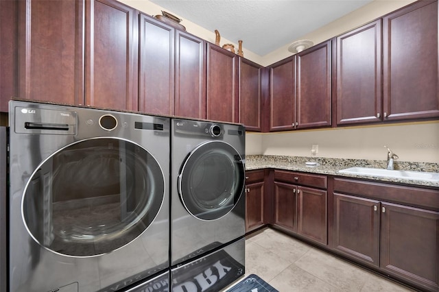 clothes washing area featuring cabinets, a textured ceiling, sink, light tile patterned floors, and washing machine and clothes dryer