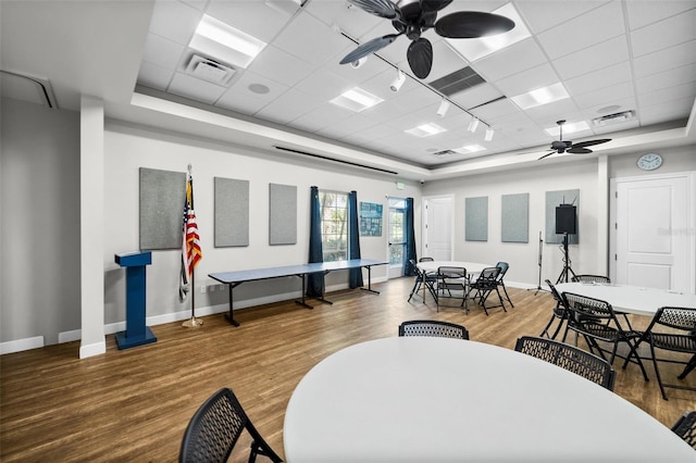 interior space with a raised ceiling, ceiling fan, hardwood / wood-style floors, and a drop ceiling