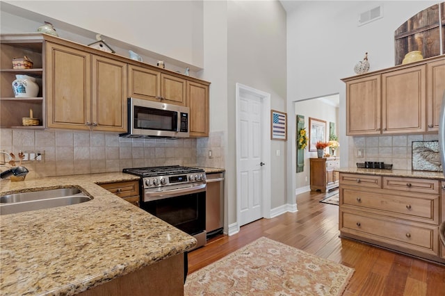 kitchen featuring sink, decorative backsplash, light stone countertops, light wood-type flooring, and appliances with stainless steel finishes