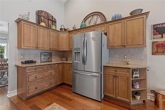 kitchen featuring light stone countertops, stainless steel fridge with ice dispenser, tasteful backsplash, and hardwood / wood-style floors