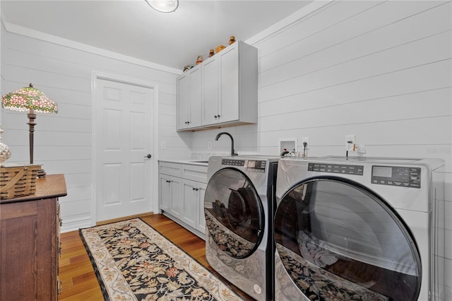 laundry area featuring cabinets, sink, wooden walls, washer and dryer, and light wood-type flooring