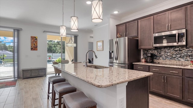 kitchen featuring stainless steel appliances, hanging light fixtures, a center island with sink, and sink