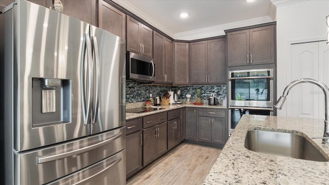 kitchen with sink, light stone counters, light wood-type flooring, appliances with stainless steel finishes, and ornamental molding