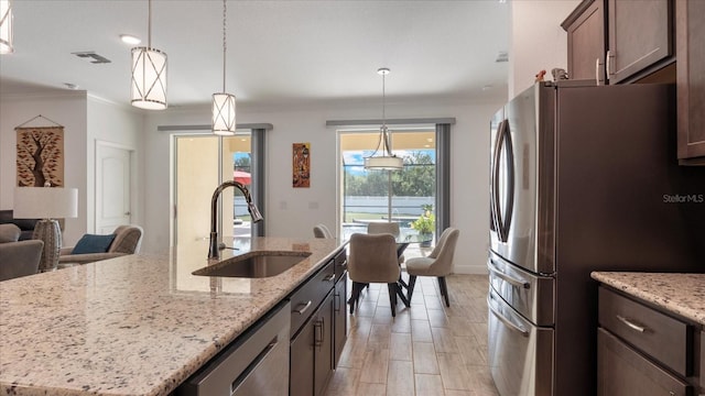 kitchen featuring sink, light stone counters, a center island with sink, appliances with stainless steel finishes, and ornamental molding