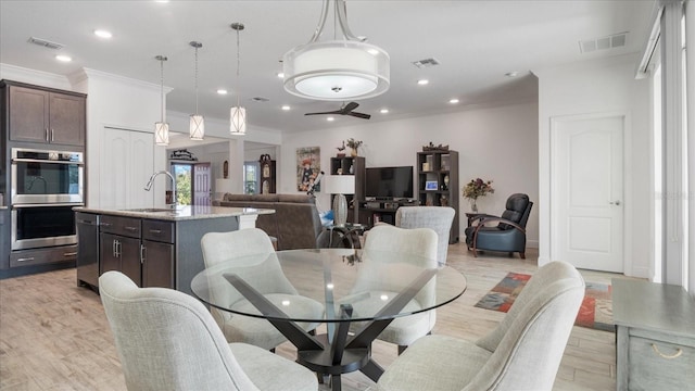 dining room featuring sink, ornamental molding, and light hardwood / wood-style flooring