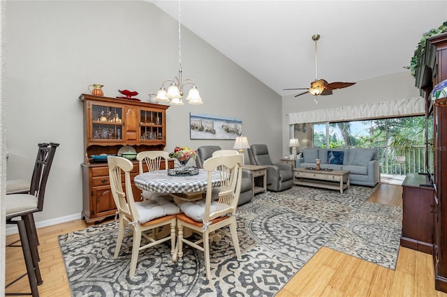 dining space with ceiling fan with notable chandelier, light wood-type flooring, and high vaulted ceiling