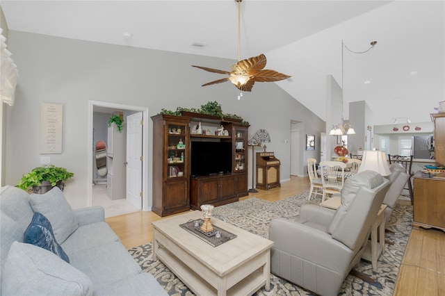 living room featuring ceiling fan with notable chandelier, high vaulted ceiling, and light hardwood / wood-style flooring