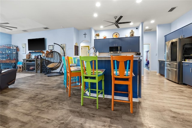 kitchen with a kitchen breakfast bar, light hardwood / wood-style flooring, ceiling fan, blue cabinetry, and stainless steel appliances