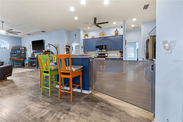 kitchen featuring hardwood / wood-style floors, ceiling fan, blue cabinetry, appliances with stainless steel finishes, and a kitchen bar