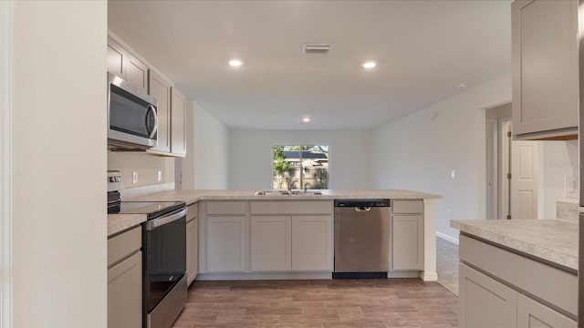 kitchen with kitchen peninsula, hardwood / wood-style flooring, sink, and appliances with stainless steel finishes