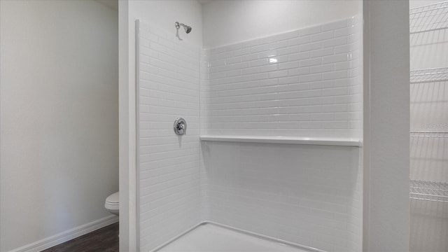 bathroom with wood-type flooring, a tile shower, and toilet