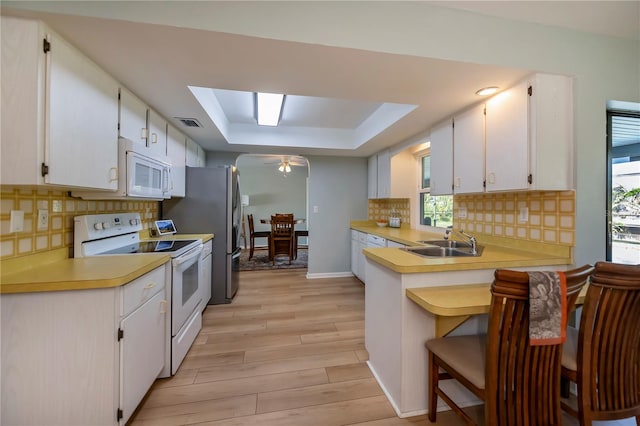 kitchen featuring a kitchen bar, white appliances, a tray ceiling, sink, and white cabinets