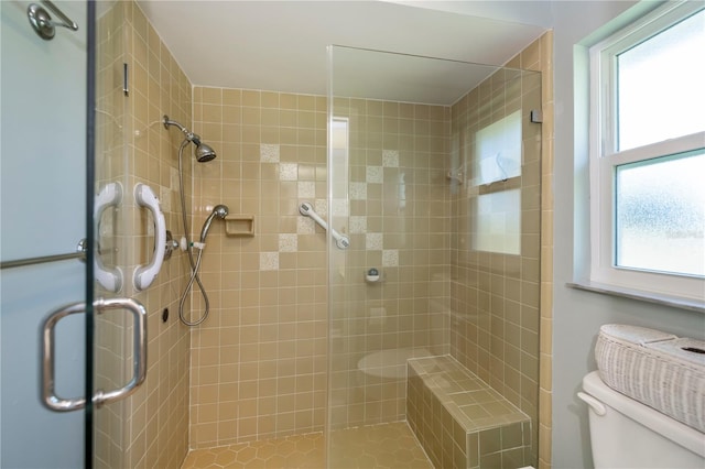 bathroom with tile patterned flooring, toilet, a shower with door, and a healthy amount of sunlight