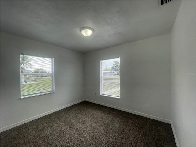 spare room featuring a wealth of natural light and dark colored carpet