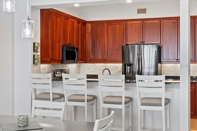 kitchen featuring sink, stainless steel fridge, pendant lighting, a kitchen bar, and decorative backsplash