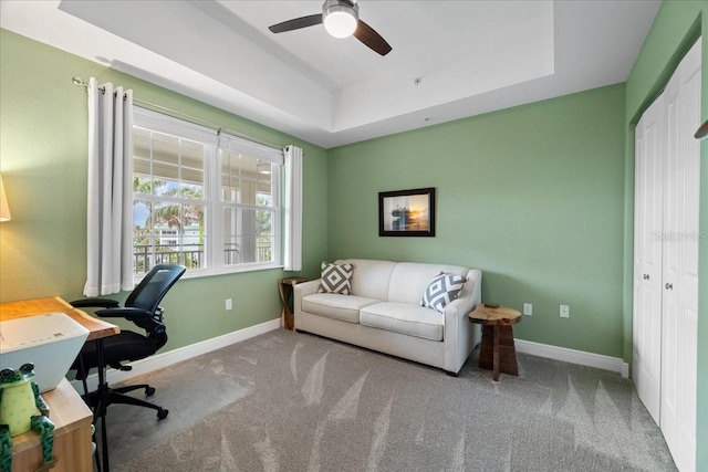 carpeted home office featuring ceiling fan and a raised ceiling