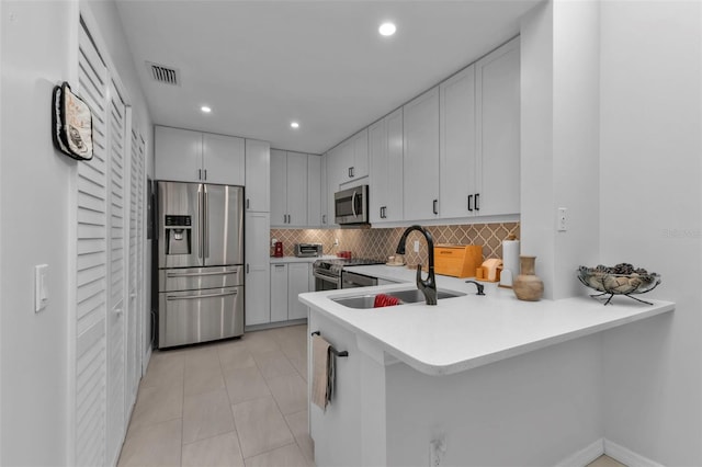 kitchen with white cabinetry, sink, kitchen peninsula, decorative backsplash, and appliances with stainless steel finishes