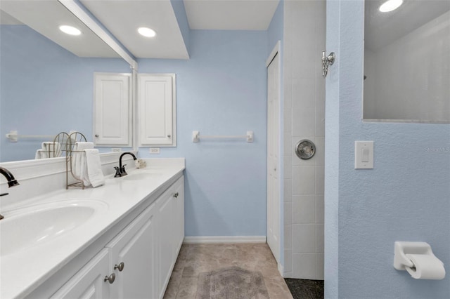 bathroom with a sink, baseboards, double vanity, and a tile shower