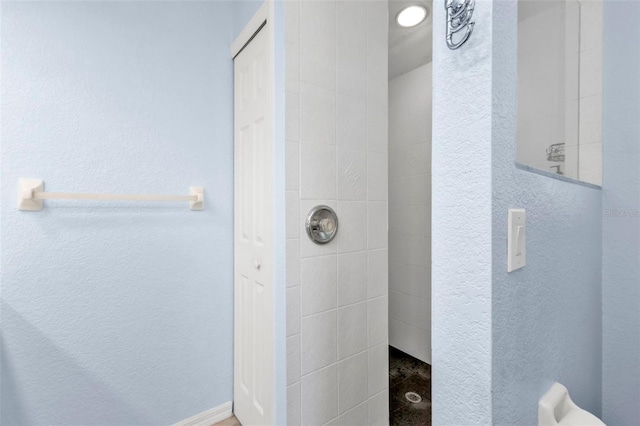 full bath featuring tiled shower and a textured wall