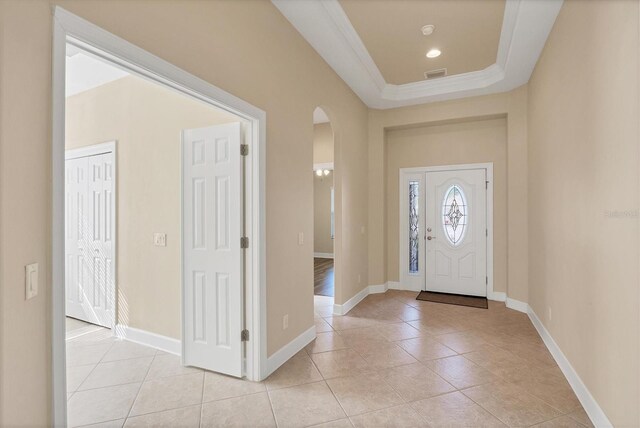 tiled entrance foyer with a tray ceiling and ornamental molding