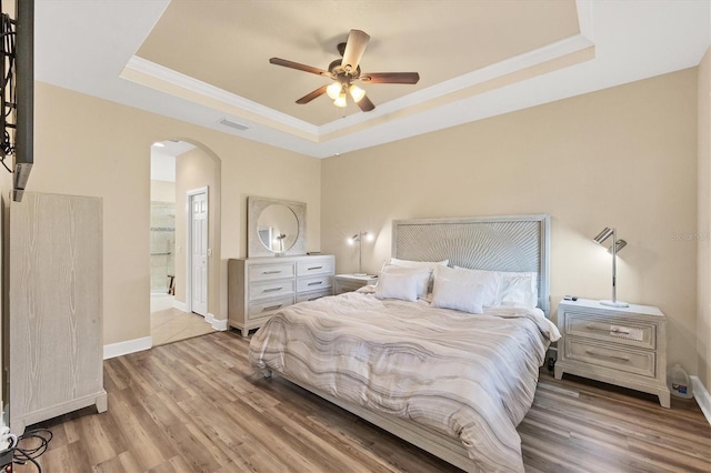 bedroom with ceiling fan, a tray ceiling, connected bathroom, and light hardwood / wood-style flooring