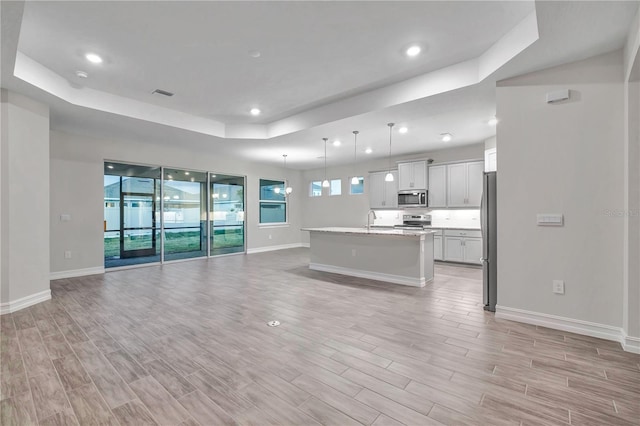 unfurnished living room with a raised ceiling, sink, and light hardwood / wood-style floors