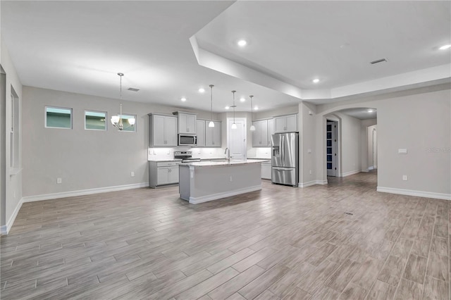 kitchen with light hardwood / wood-style flooring, stainless steel appliances, hanging light fixtures, and an island with sink